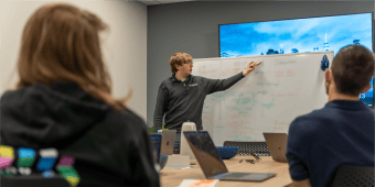 A man in a conference room explaining something white a whiteboard